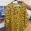 Yellow dress with black polka dots and orange sunflowers on a black hanger, held by a hand, button-front detail visible.