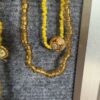 Yellow beaded necklace with a round gold filigree pendant resting on gray fabric, shown in close-up.