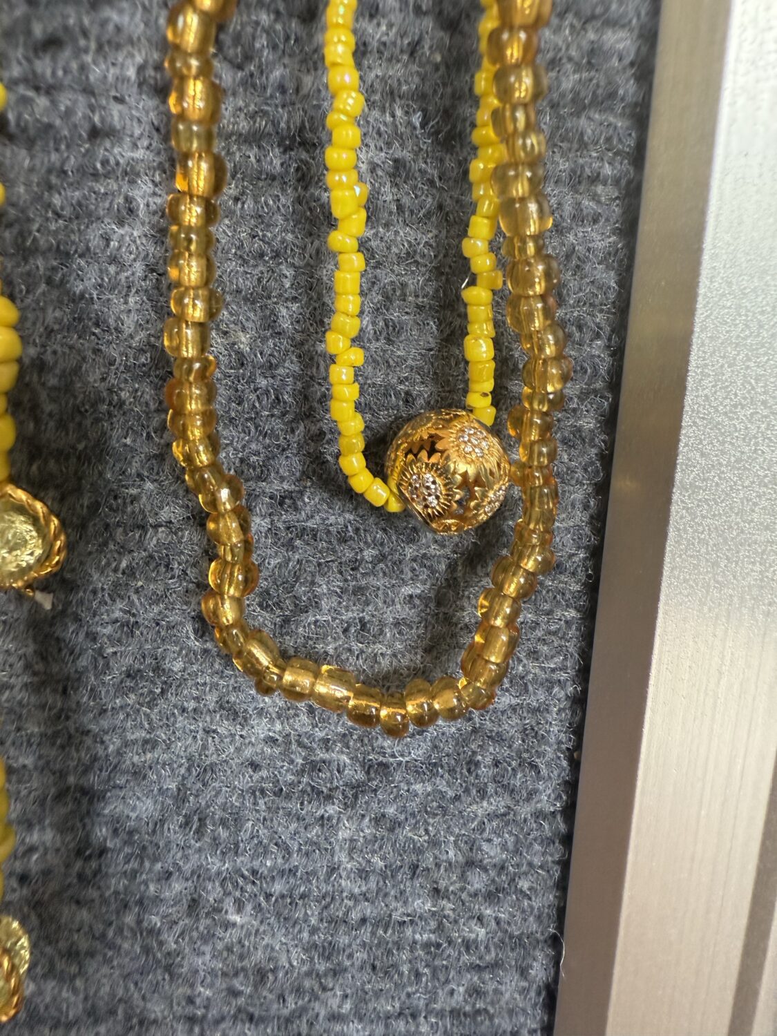 Yellow beaded necklace with a round gold filigree pendant resting on gray fabric, shown in close-up.