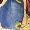 Blue denim jeans folded on a bed with bright sunflower embroidery on the back pocket and upper thigh area.