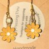 sunflowers Handmade gold-tone earrings with yellow daisy charms and white centers, mounted on a beige display card