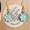 blue daisies Pair of turquoise daisy pendant earrings with yellow centers on gold hooks, displayed on a brown card.