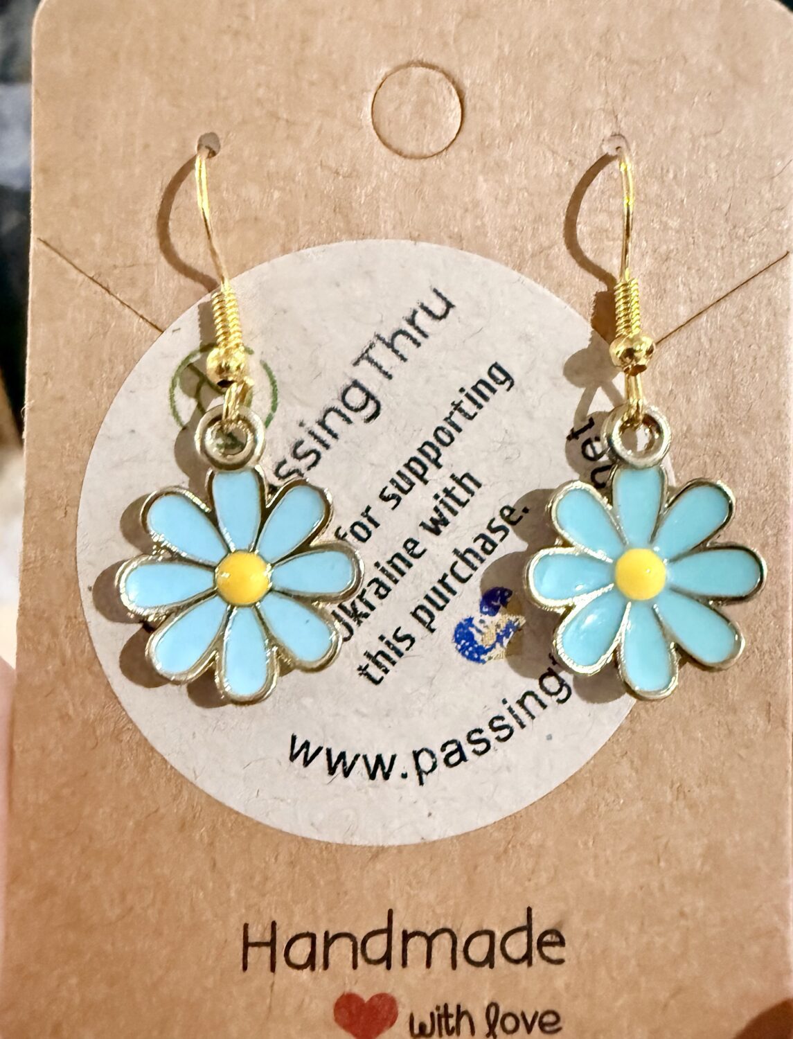 blue daisies Pair of turquoise daisy pendant earrings with yellow centers on gold hooks, displayed on a brown card.