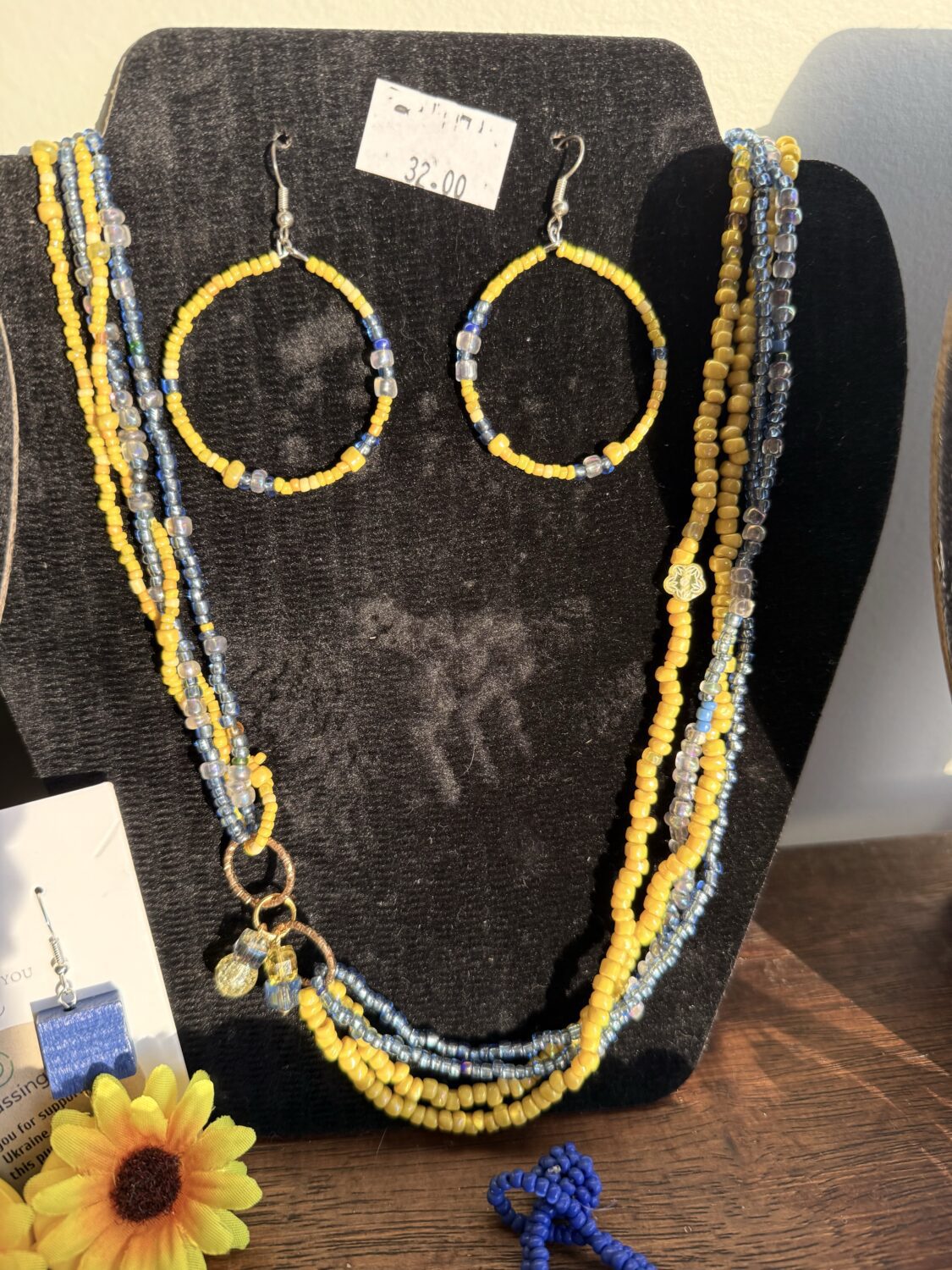 Beaded yellow and blue jewelry set on a black display board, featuring large circular hoop earrings and multiple bead strands with a price tag above.