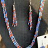 Multi-strand beaded necklace in red, blue, and turquoise with silver bell charms; matching beaded earrings on a black display bust.