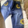 Blue denim jeans with large sunflower embroidery on back pocket and leg pocket detail, laid out on a couch.