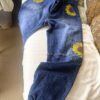 Blue denim jeans with sunflower embroidery on the back and leg pockets laid on a bedspread.