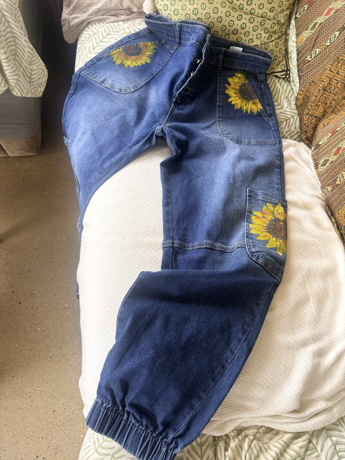 Blue denim jeans with sunflower embroidery on the back and leg pockets laid on a bedspread.