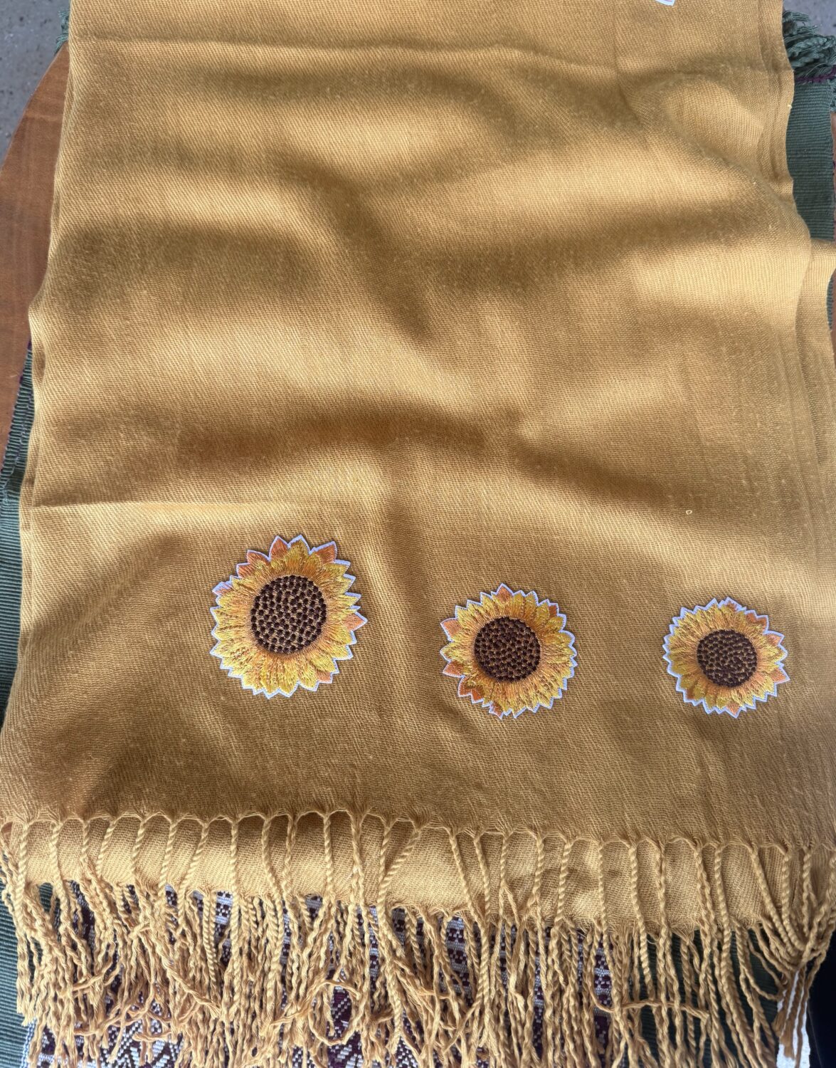 Mustard-yellow scarf with three embroidered sunflowers near the bottom edge and a fringed hem.
