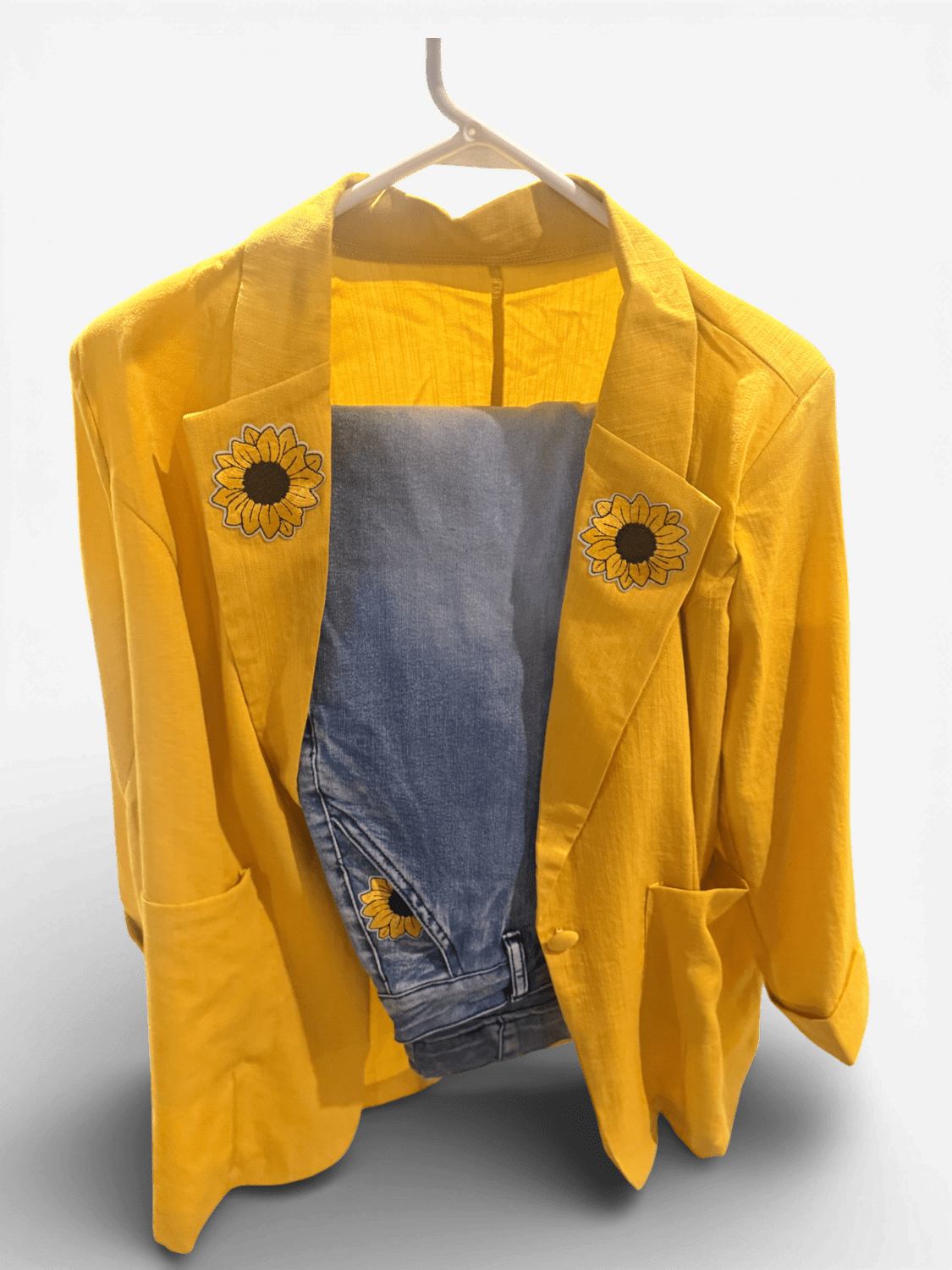 Bright yellow blazer on a hanger with denim inner lining and sunflower patches on the lapels.