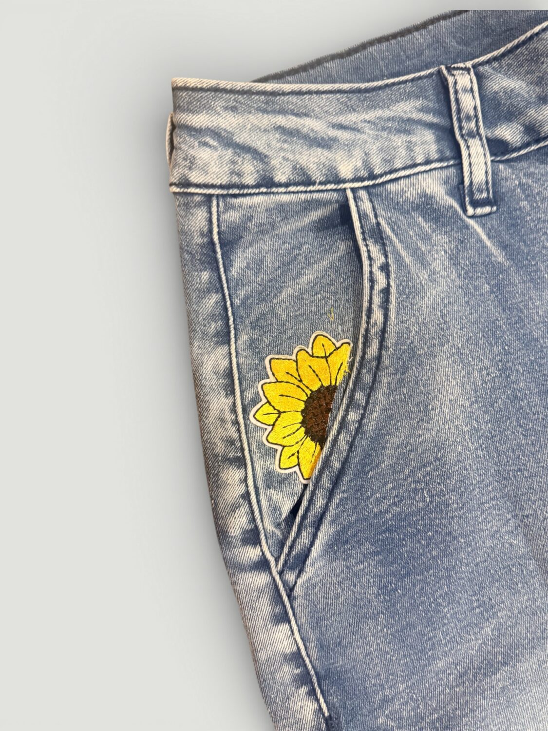 Blue denim jeans with a yellow sunflower embroidery on the front pocket area.
