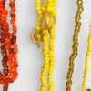 Close-up of colorful beaded necklaces in yellow, orange, and gold with round gold pendants hanging among the beads.