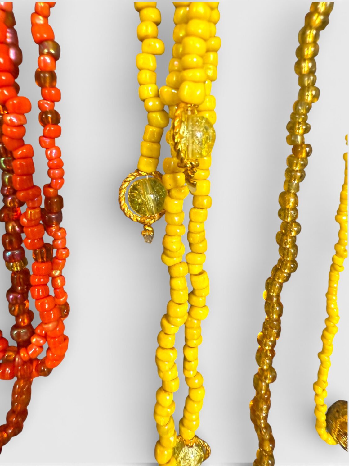 Close-up of colorful beaded necklaces in yellow, orange, and gold with round gold pendants hanging among the beads.