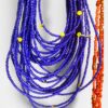 Multiple cobalt blue beaded necklaces with yellow spacers and a sunflower pendant, orange beaded strand at right for contrast.