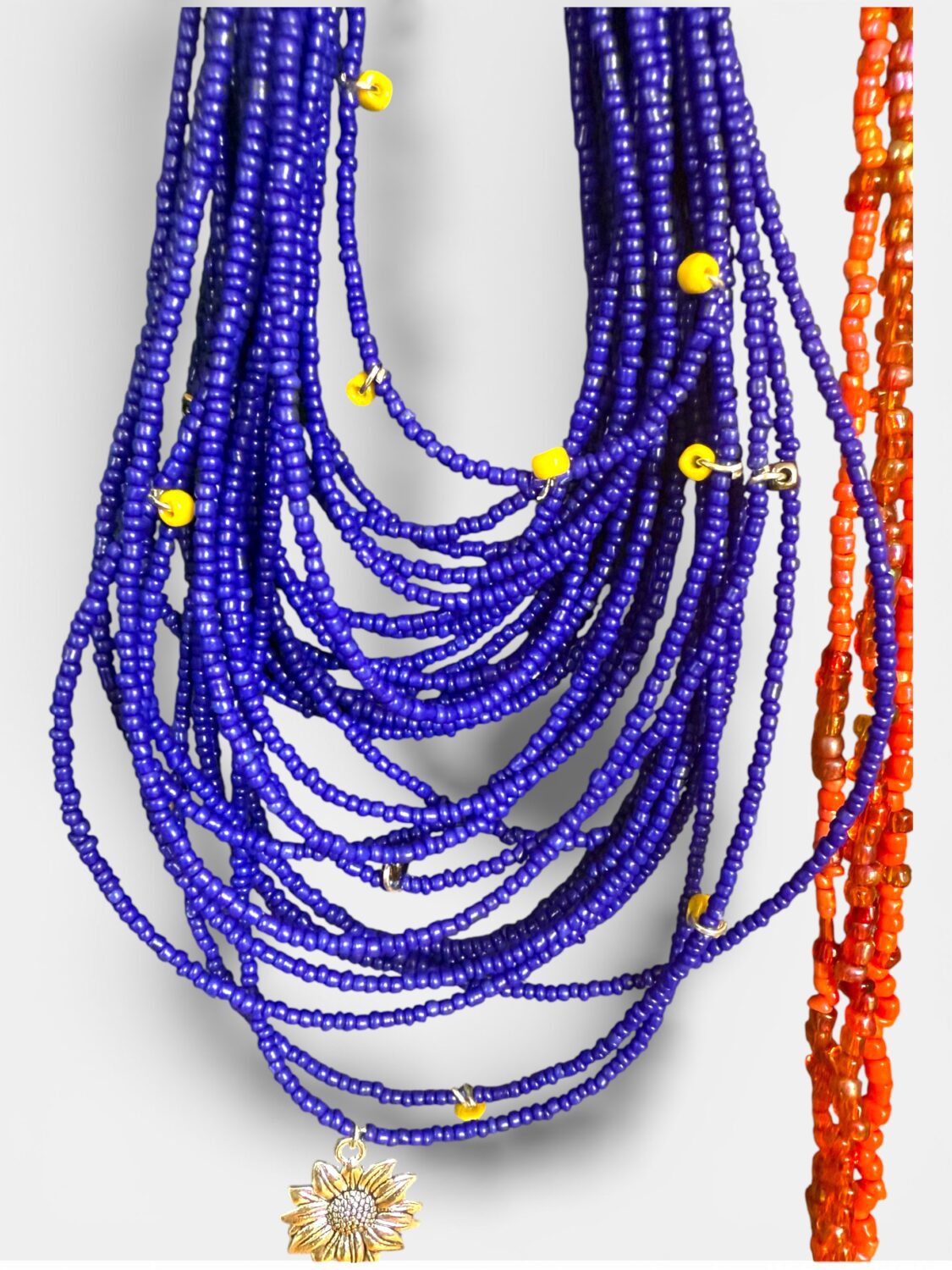 Multiple cobalt blue beaded necklaces with yellow spacers and a sunflower pendant, orange beaded strand at right for contrast.