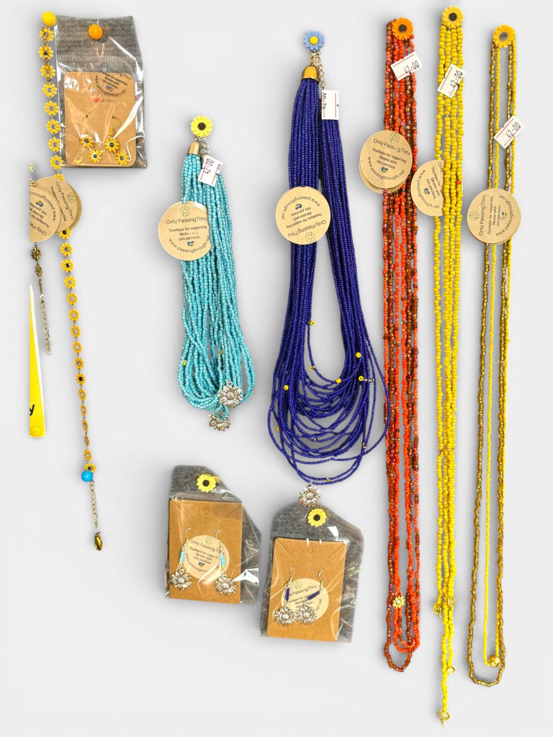 Assorted beaded jewelry: turquoise, cobalt blue, red, orange, and yellow necklaces and bracelets laid out on a white surface, some in packaging.