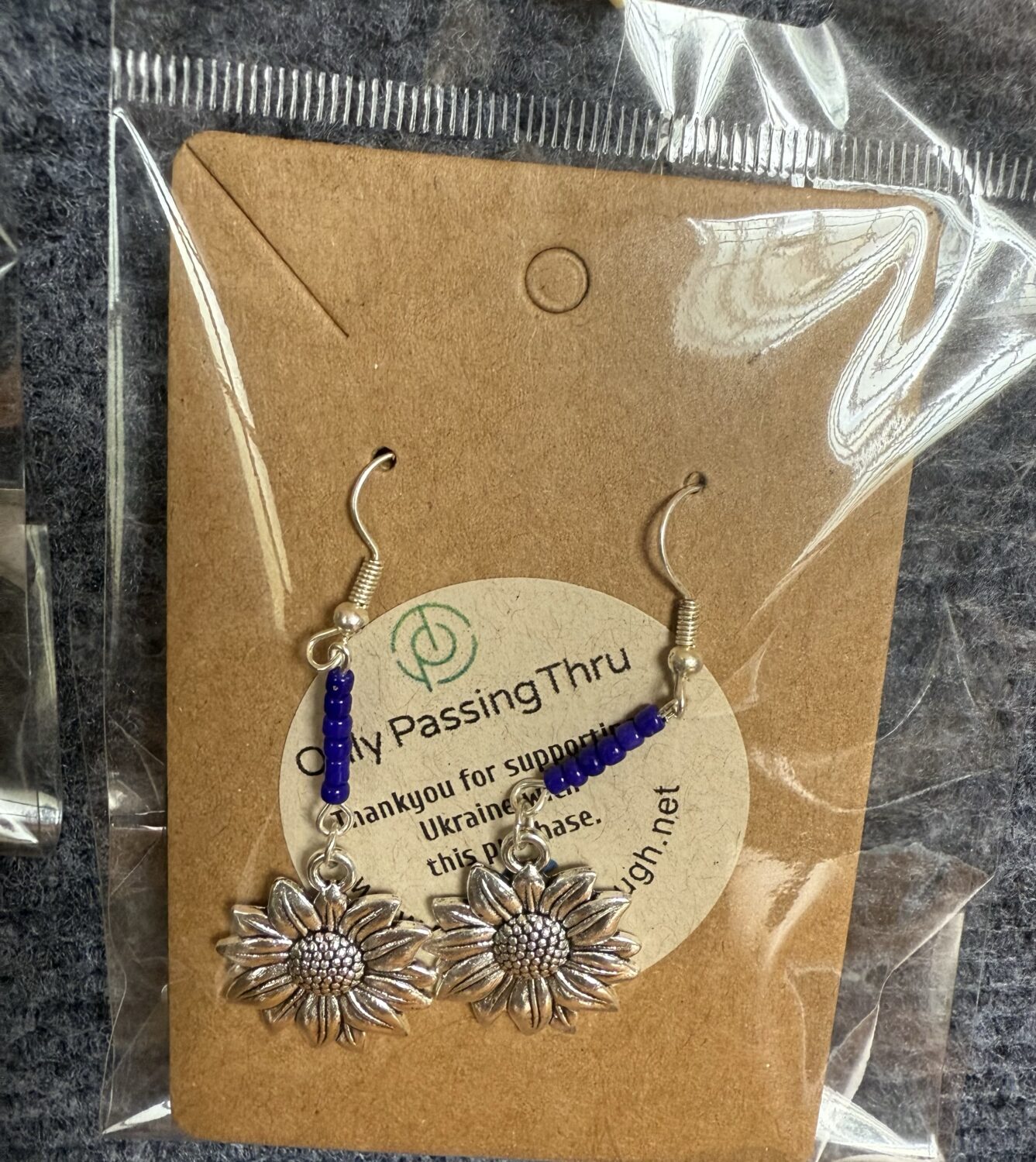 Silver sunflower drop earrings with blue/purple beads, mounted on brown kraft backing