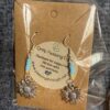 Silver sunflower-shaped earrings with blue and yellow beads, displayed on brown backing inside a plastic package.