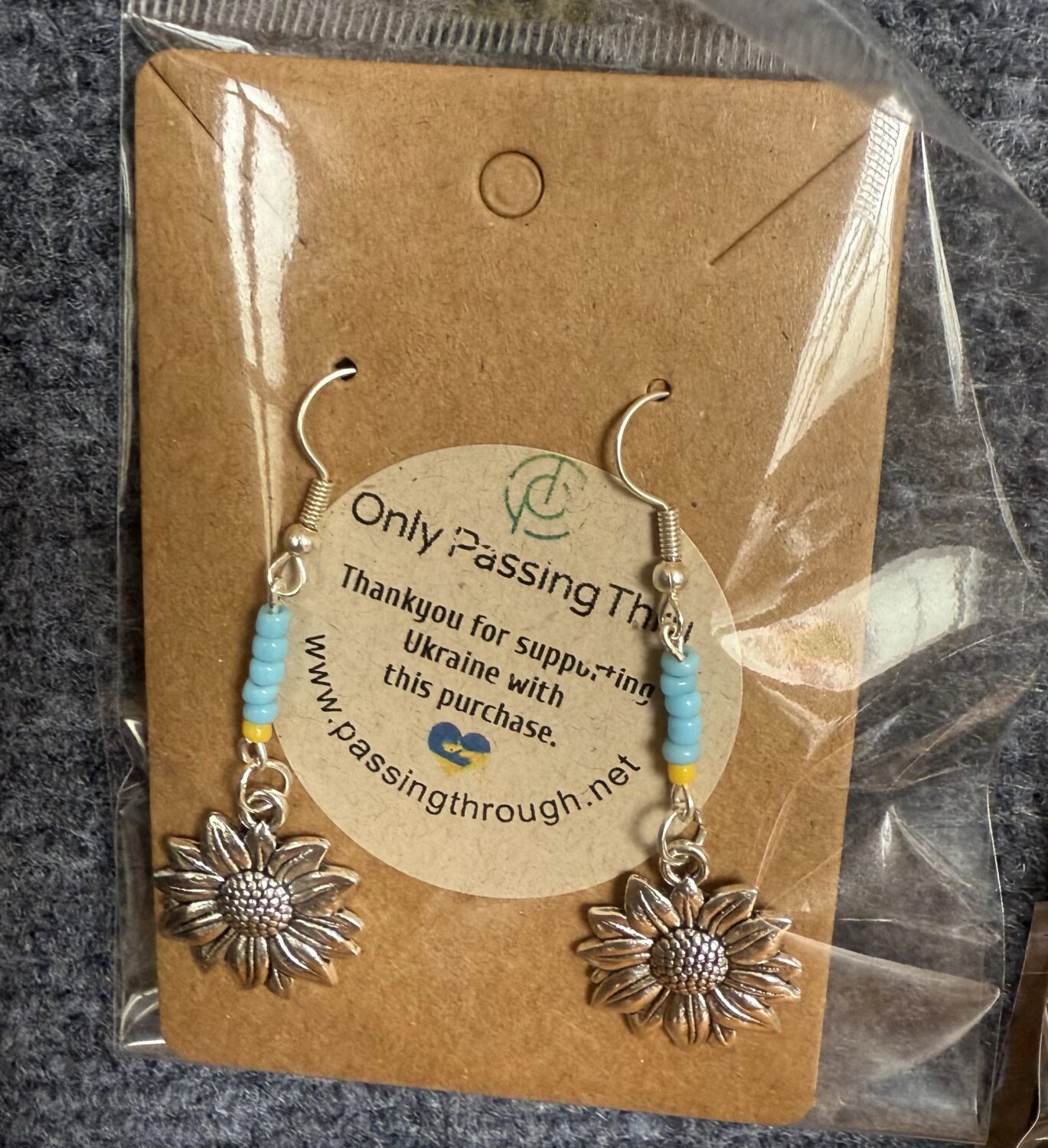 Silver sunflower-shaped earrings with blue and yellow beads, displayed on brown backing inside a plastic package.