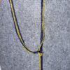 Blue and yellow beaded necklace draped in a U-shape with a knot and hanging strands on a gray fabric background.
