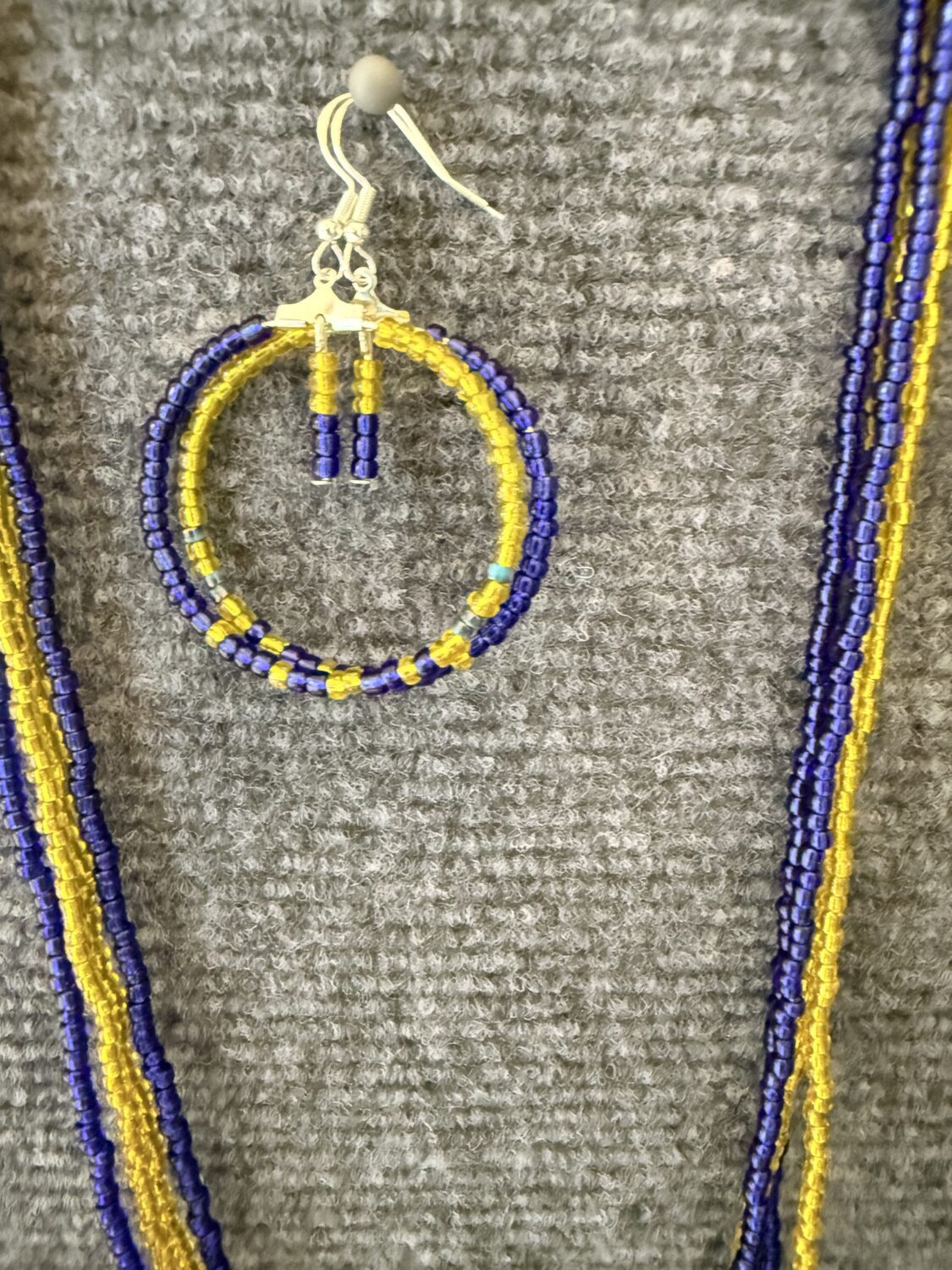Beaded hoop earring in purple and yellow with a small bead-figure charm hanging from the top, surrounded by matching bead strands.