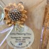 Gold-tone sunflower brooch with crystal-studded center and petal details, in plastic packaging.