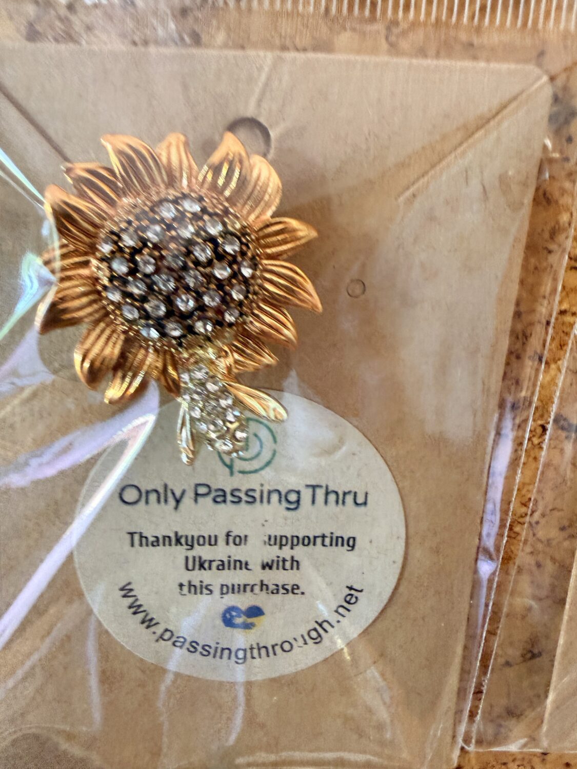 Gold-tone sunflower brooch with crystal-studded center and petal details, in plastic packaging.