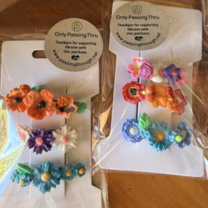 Colorful flower hair clips on white display cards in clear packaging, with a 'Only PassingThru' support Ukraine label.