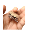 Hand holding a small round cosmetic container with a beige foil seal and a clear base between fingers, against a green background.