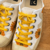 White canvas sneakers with bright yellow laces and sunflower print on a wooden surface.
