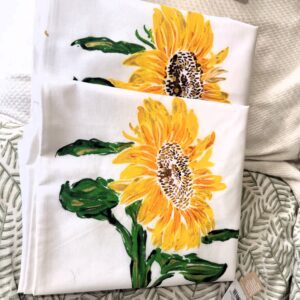 White fabric featuring a bright sunflower print with yellow petals and green leaves, folded in layers.