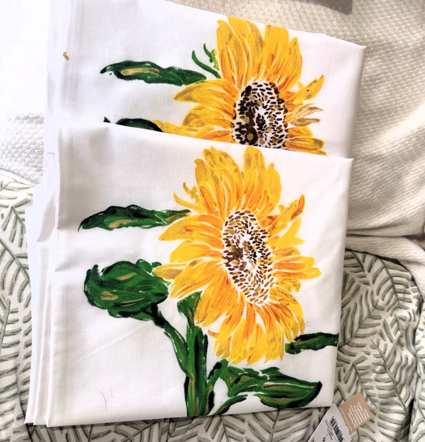 White fabric featuring a bright sunflower print with yellow petals and green leaves, folded in layers.