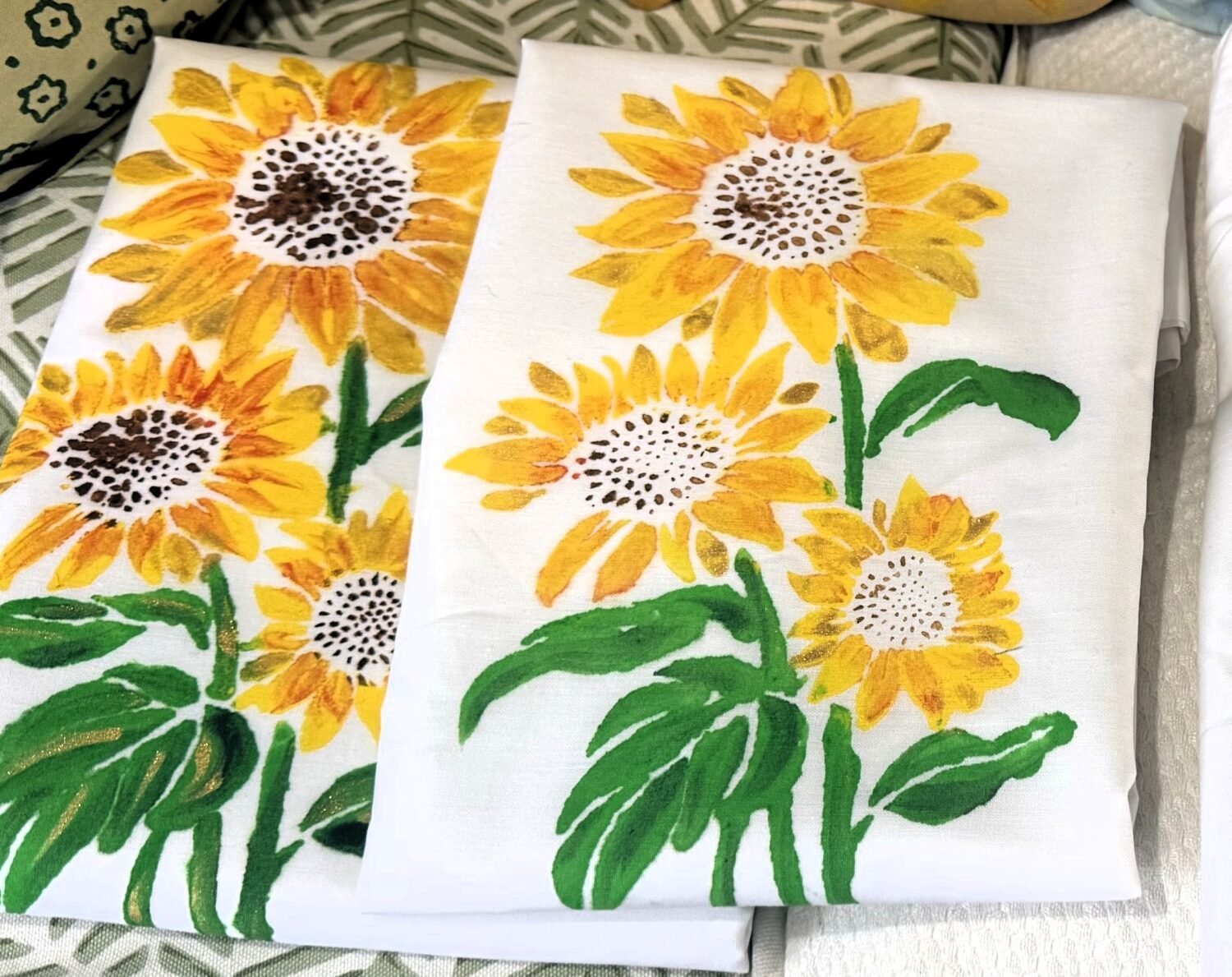 White fabric with bright sunflower print: yellow petals, brown centers, and green stems on a white background (decorative textiles).