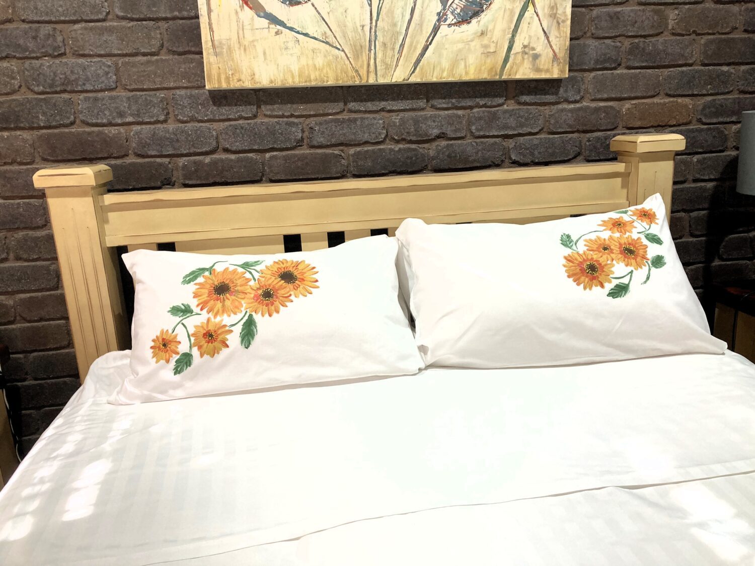 Wooden bed frame against a dark brick wall with white bedding and sunflower-patterned pillows.