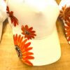 White baseball cap with bright orange sunflower-like flowers painted on the brim and side panels.