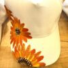 White baseball cap with orange sunflower print along the brim and side surface.