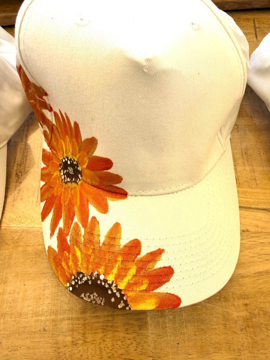 White baseball cap with orange sunflower print along the brim and side surface.