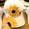 White baseball cap with bright yellow sunflower prints on the front and brim, placed on a wooden table surface.