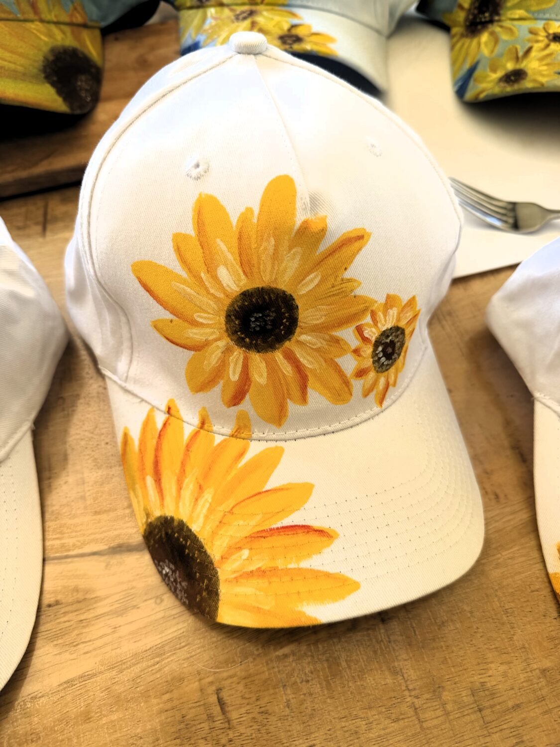 White baseball cap with bright yellow sunflower prints on the front and brim, placed on a wooden table surface.