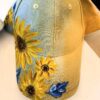 Light blue denim baseball cap with bright yellow sunflower embroidery along the front brim and side panels.