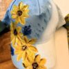 Light blue baseball cap with yellow floral embroidery along the front panel and brim edge.