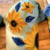 Denim baseball cap with large yellow sunflowers and dark centers on a light blue base, resting on a wooden surface.