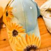 Denim baseball cap with bright sunflower prints along the brim on a wooden surface