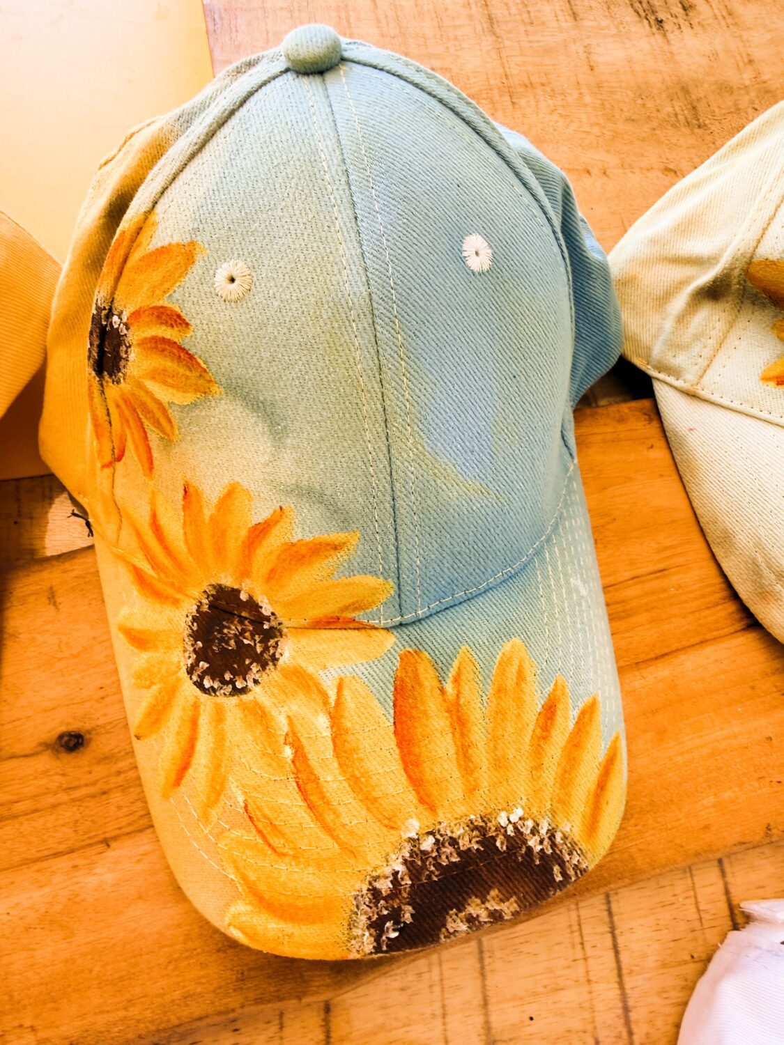 Denim baseball cap with bright sunflower prints along the brim on a wooden surface