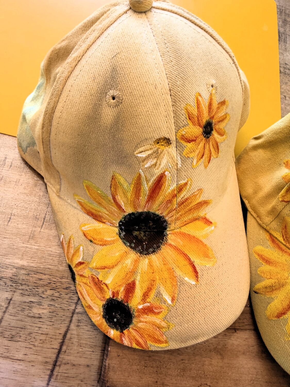 Beige cap decorated with large yellow sunflowers embroidered on the front.