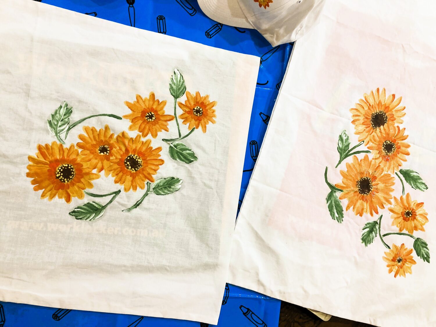 Two white fabric panels printed with bright orange sunflowers and green leaves laid on a blue surface.