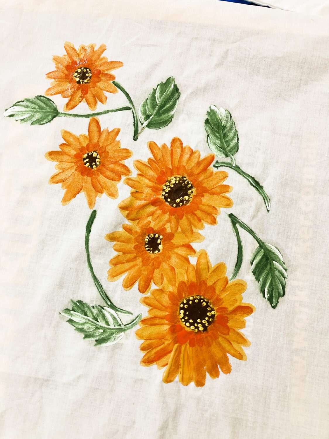Orange sunflower prints on a light fabric, with green leaves and stems interwoven among the blossoms.