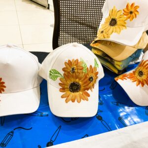 White baseball caps with large sunflower embroidery displayed on a blue table in a store.