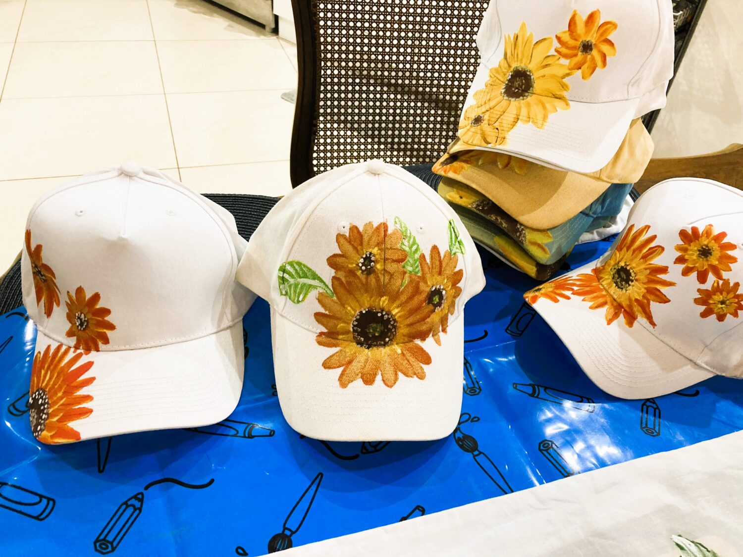 White baseball caps with large sunflower embroidery displayed on a blue table in a store.