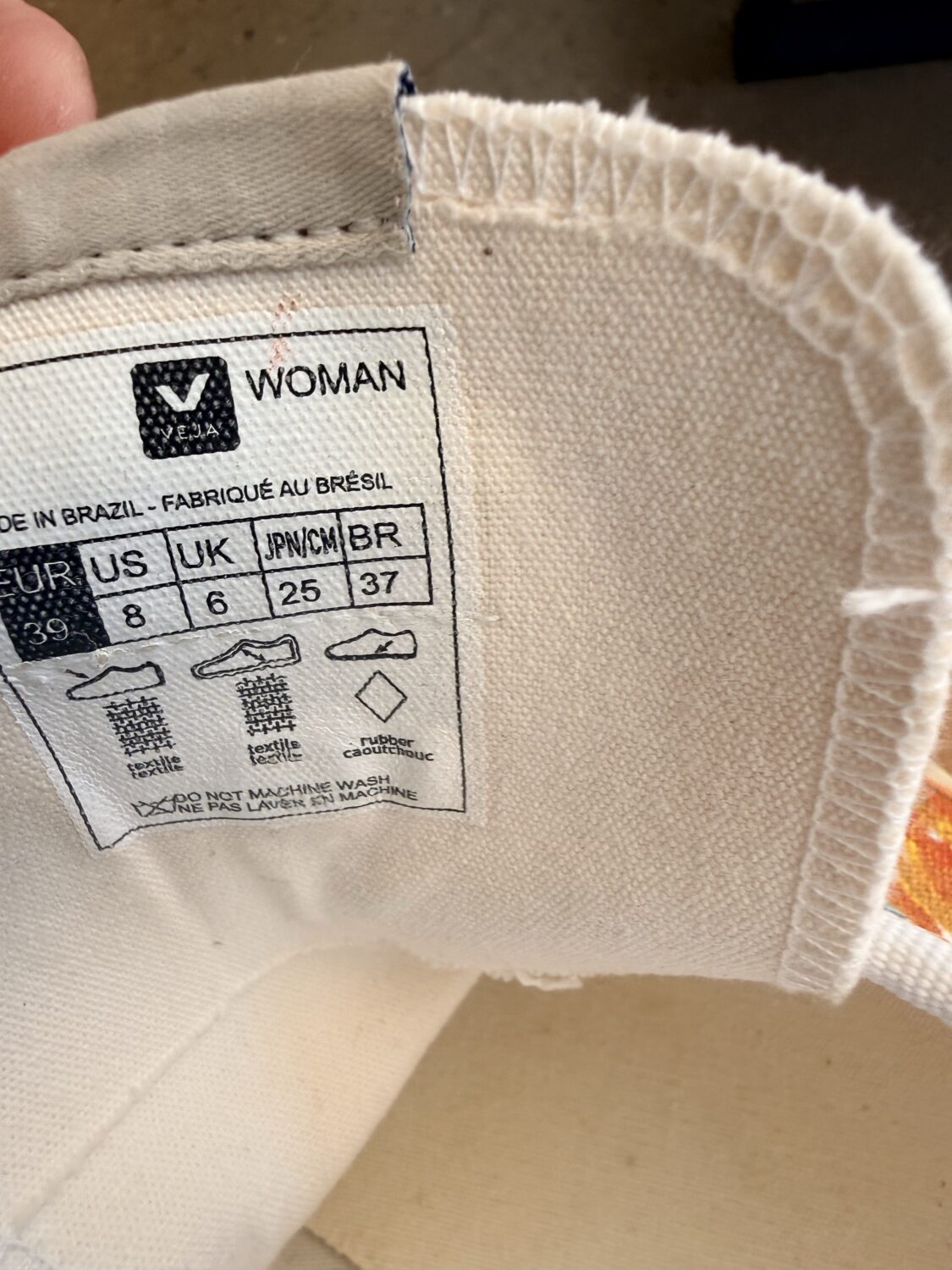 Label inside a white garment showing 'WOMAN' and size chart (US 8, UK 6, JP 25, BR 37) with care icons and 'do not machine wash' note.